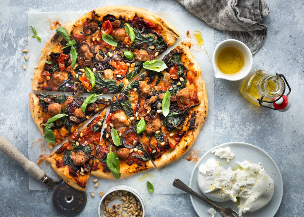 Pizza met uien, spinazie, rozijnen en stukjes worst