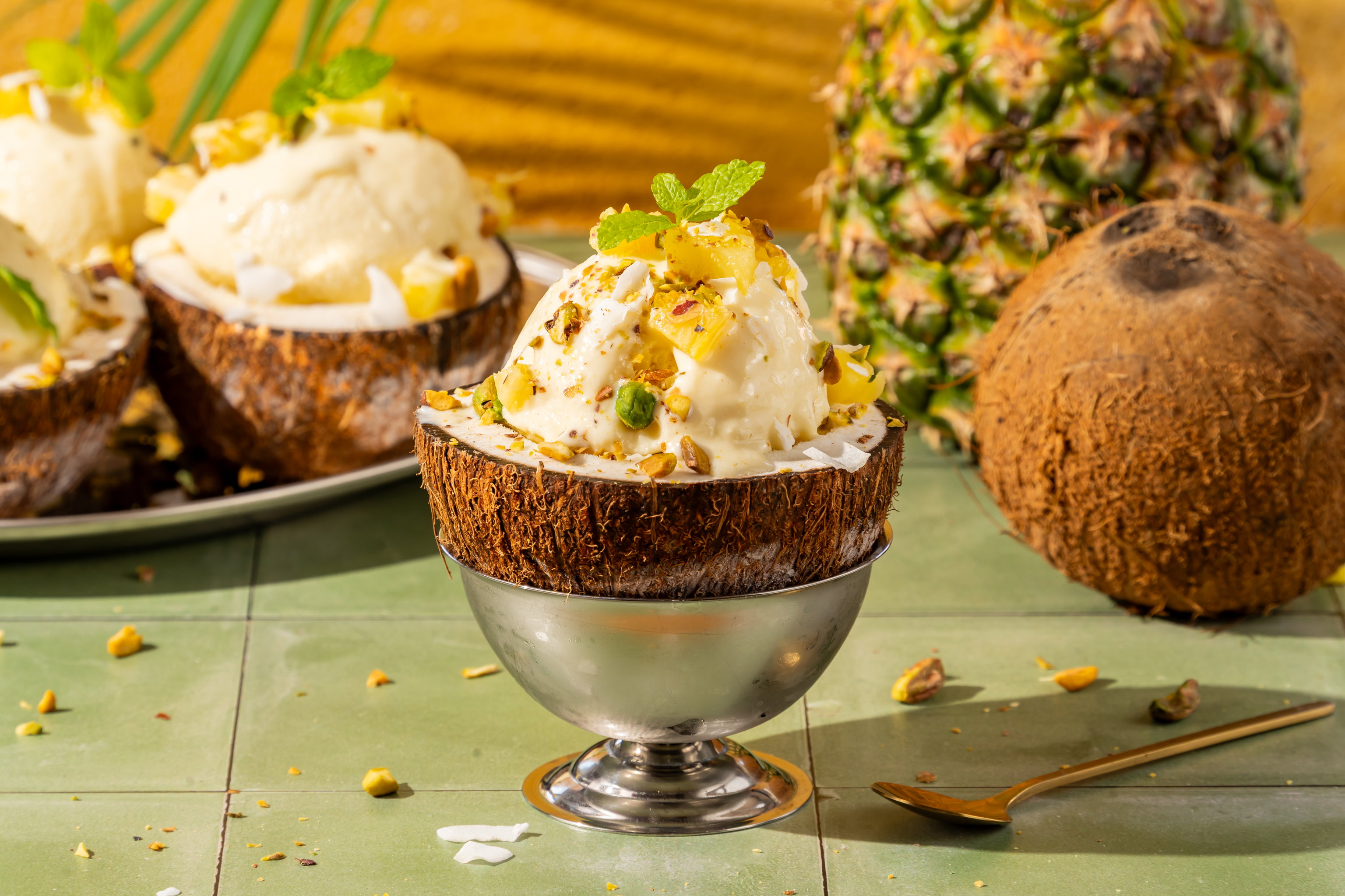 Gevulde kokosnoothelften met kokos-ananasijs, pistachenoten, verse ananas en munt.
