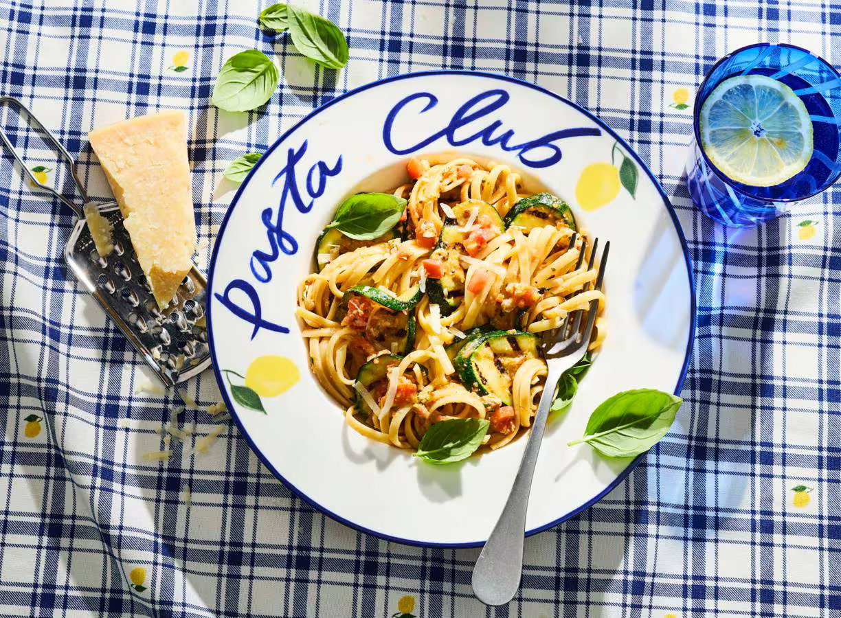 Linguine met rode pesto, geroosterde cherrytomaten, rucola, burrata en basilicum op een bord.
