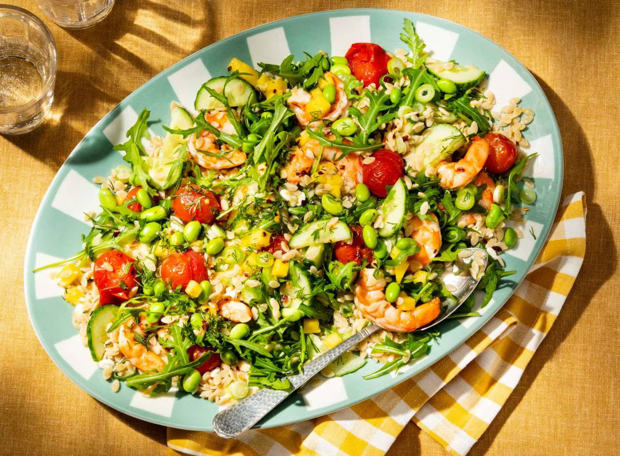 Zomerse orzosalade met garnalen, mango, edamame, cherrytomaten, komkommer en rucola in een schaal.