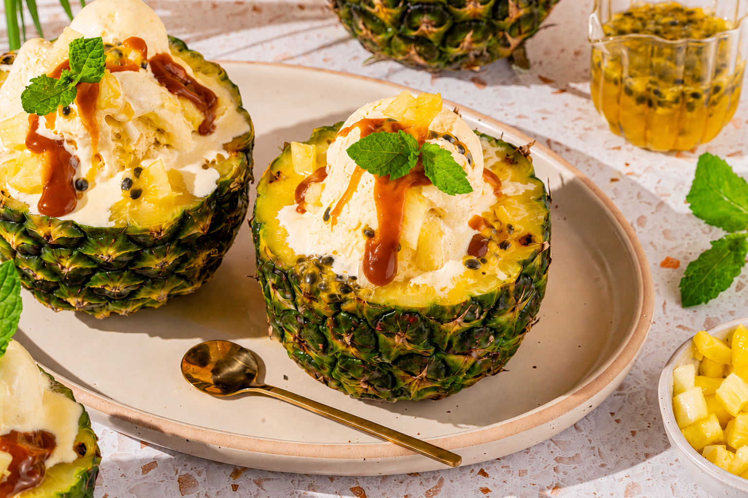 Tropisch ananasijs geserveerd in een uitgeholde ananas met passievrucht, karamelpasta en verse munt.