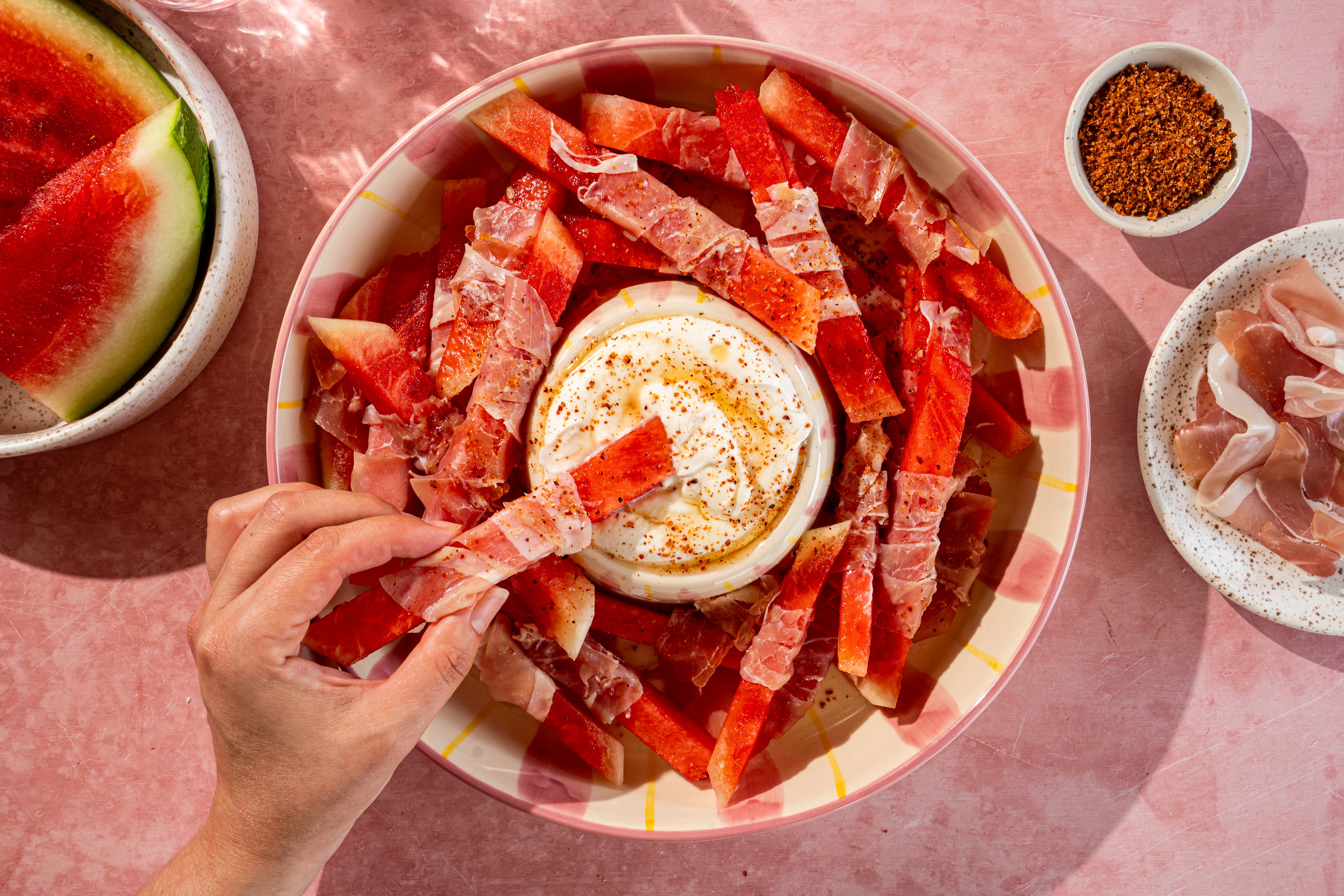 Watermeloen prosciutto bites met whipped ricotta, hot honey en tajin op een zomerse serveerschaal.