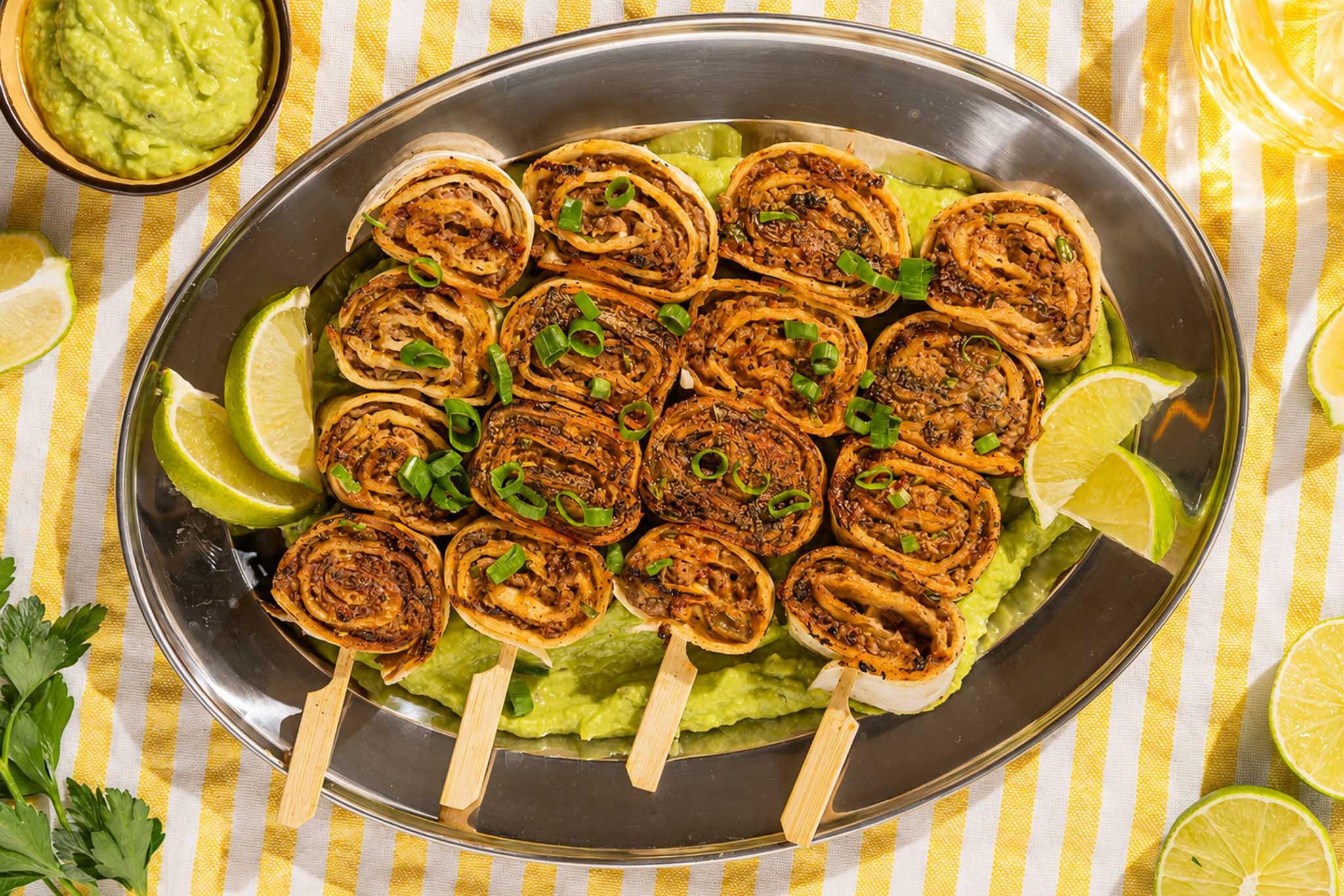 BBQ tortilla beef spiesjes met chipotle limoenboter, bosui en avocadodip op een bord.