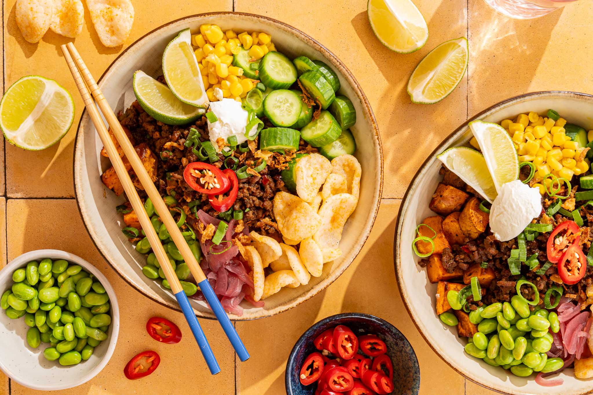 Indonesische bowl met geroosterde zoete aardappel, kruidig gehakt, edamame, maïs, komkommer, rode ui, kroepoek en limoen.