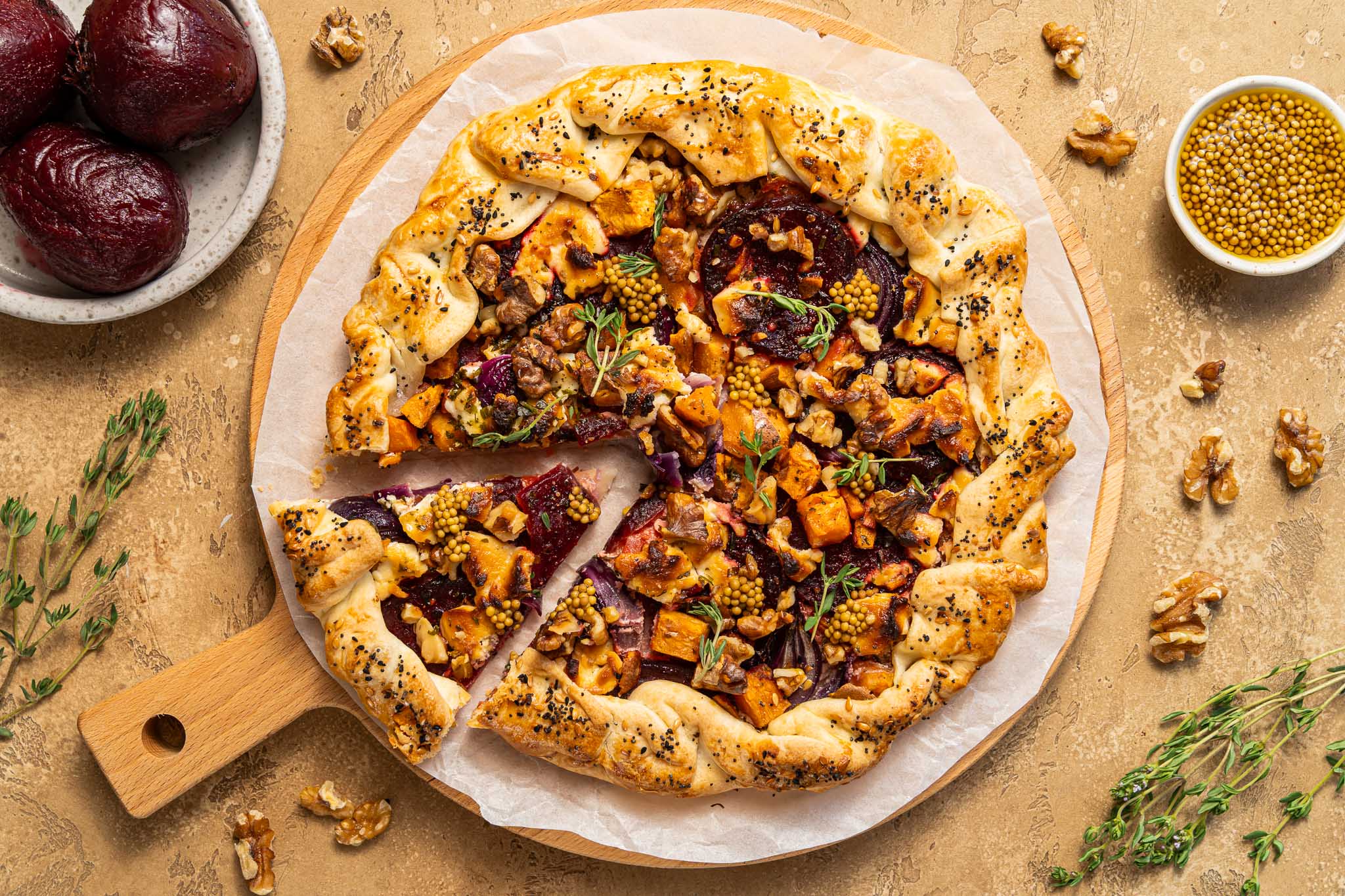Gebakken galette met rode biet, zoete aardappel, geitenkaas en kruiden op een houten plank