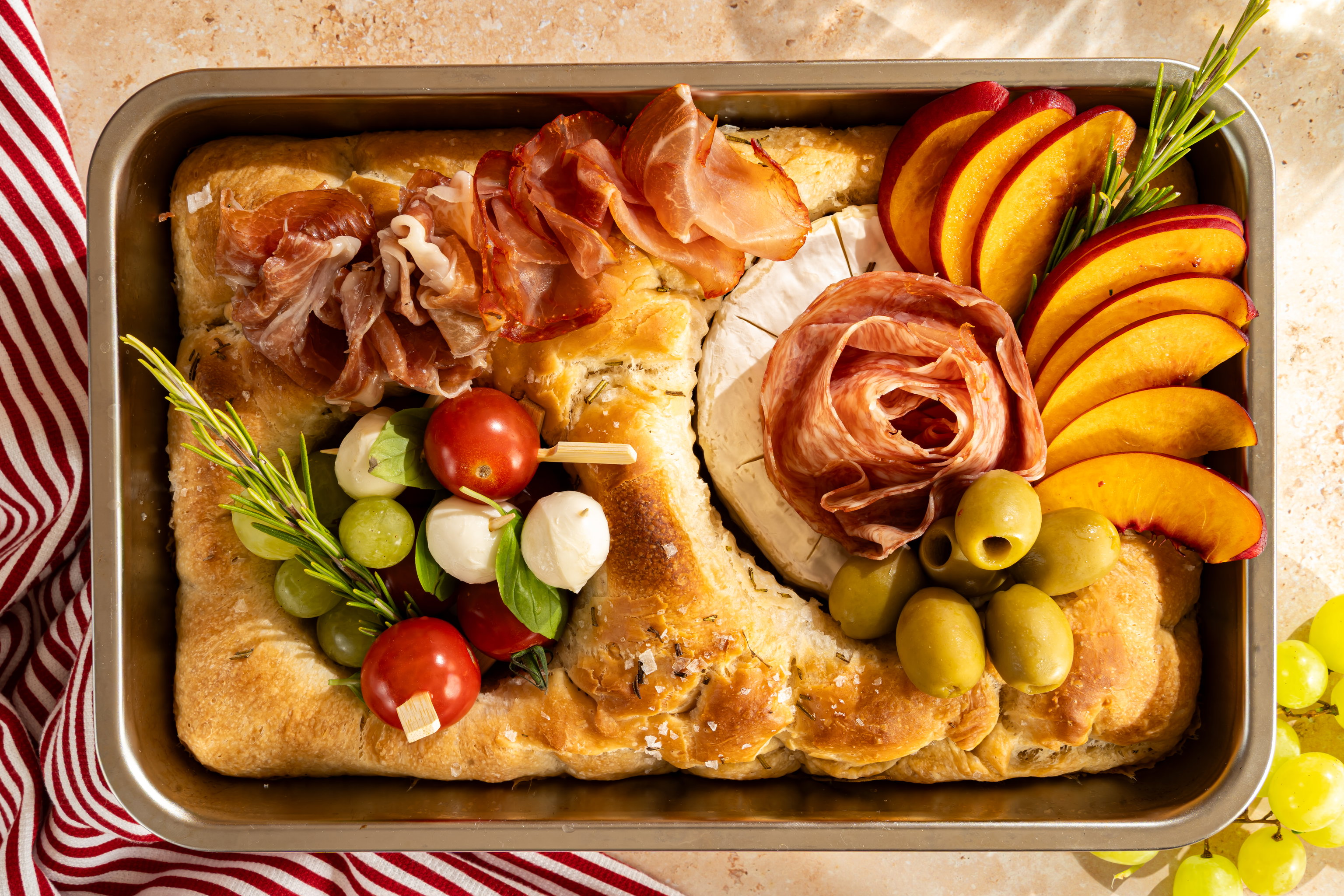 Zelfgebakken charcuterie focaccia met prosciutto, camembert, capresespiesjes, groene olijven, druiven en nectarine.