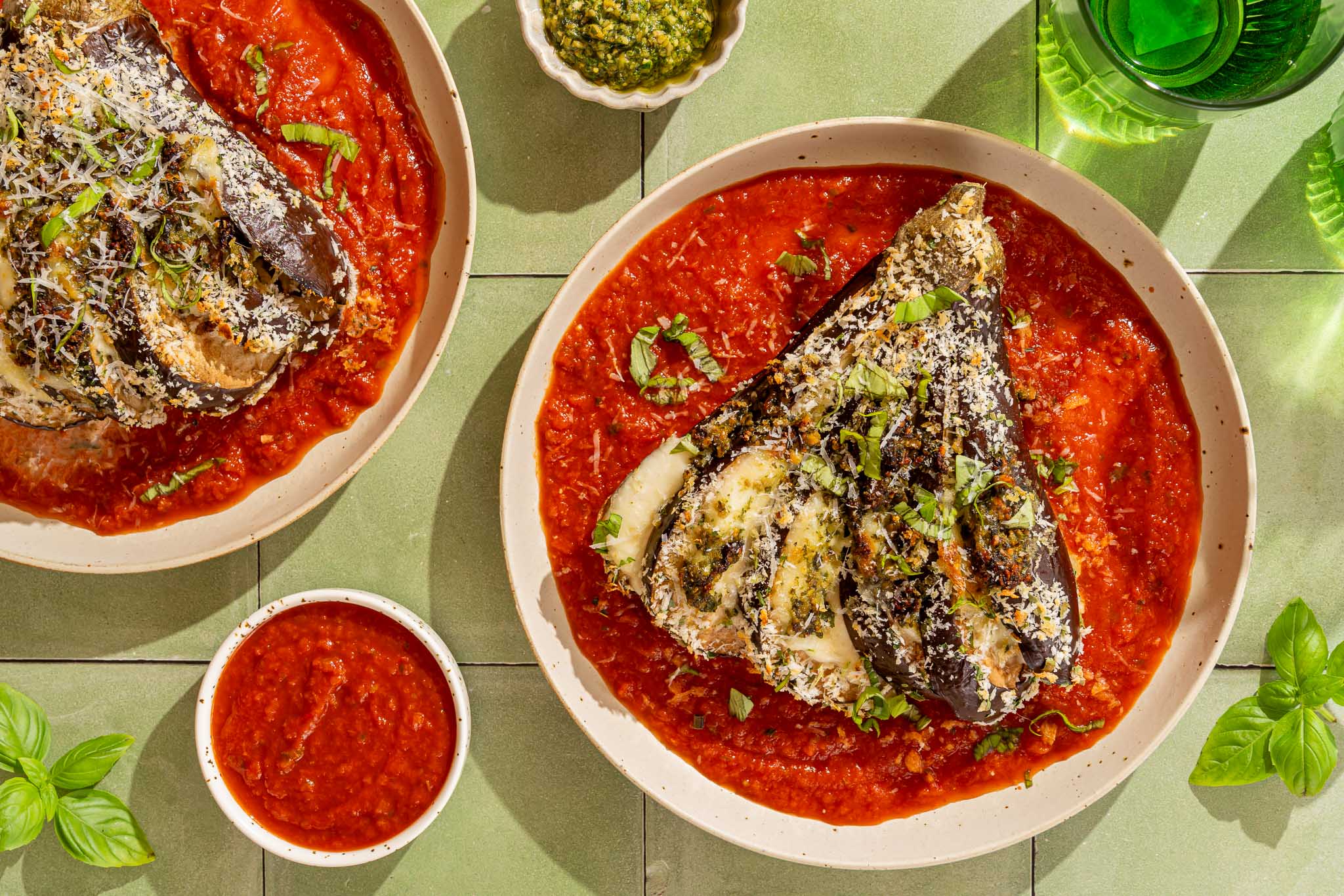 Crispy waaieraubergine gevuld met mozzarella en groene pesto, geserveerd op tomatensaus met Parmezaanse kaas en basilicum.