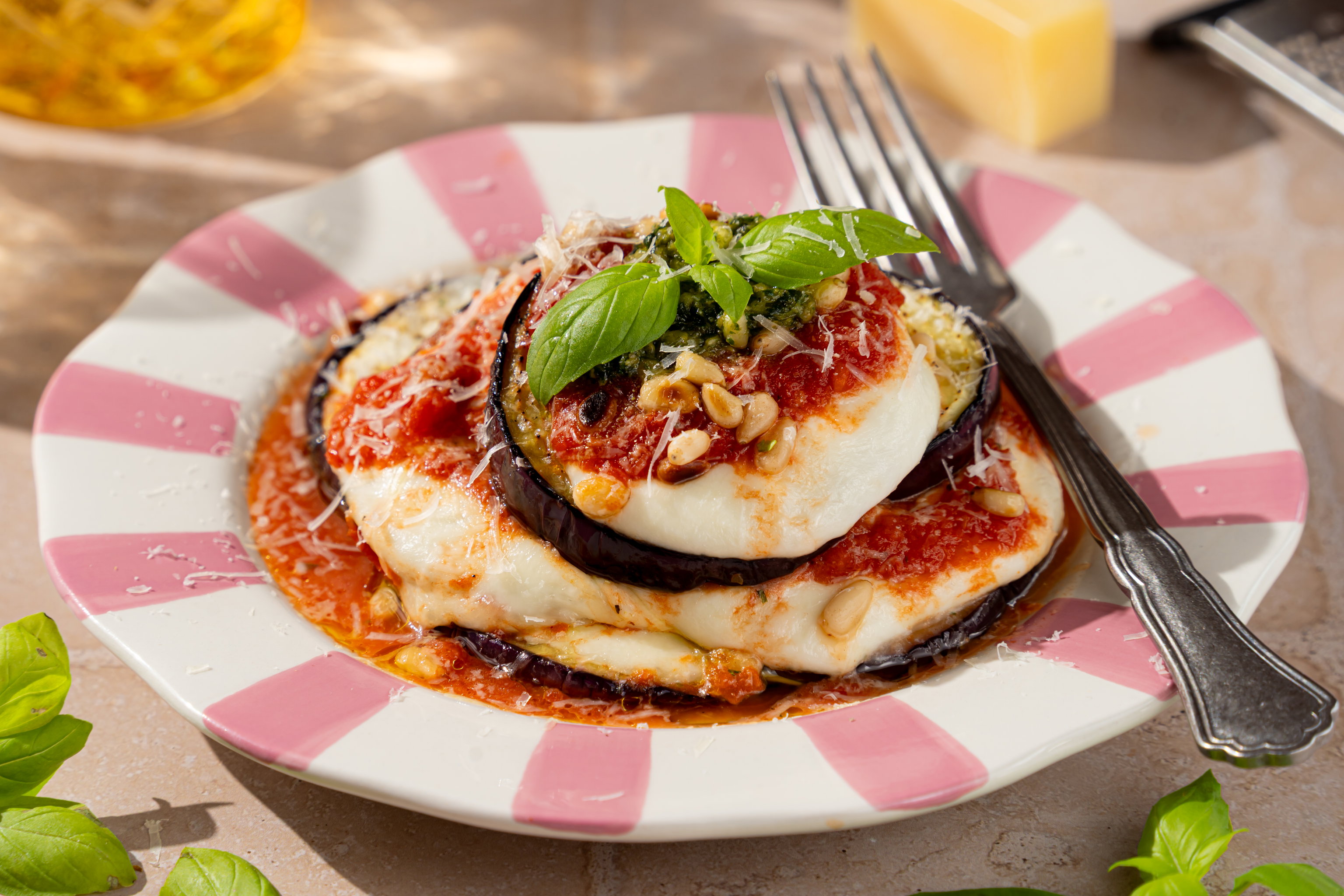 Parmigiana di melanzane met goudbruin gebakken aubergine, gesmolten mozzarella, tomatensaus, pesto, Parmezaanse kaas en basilicum.