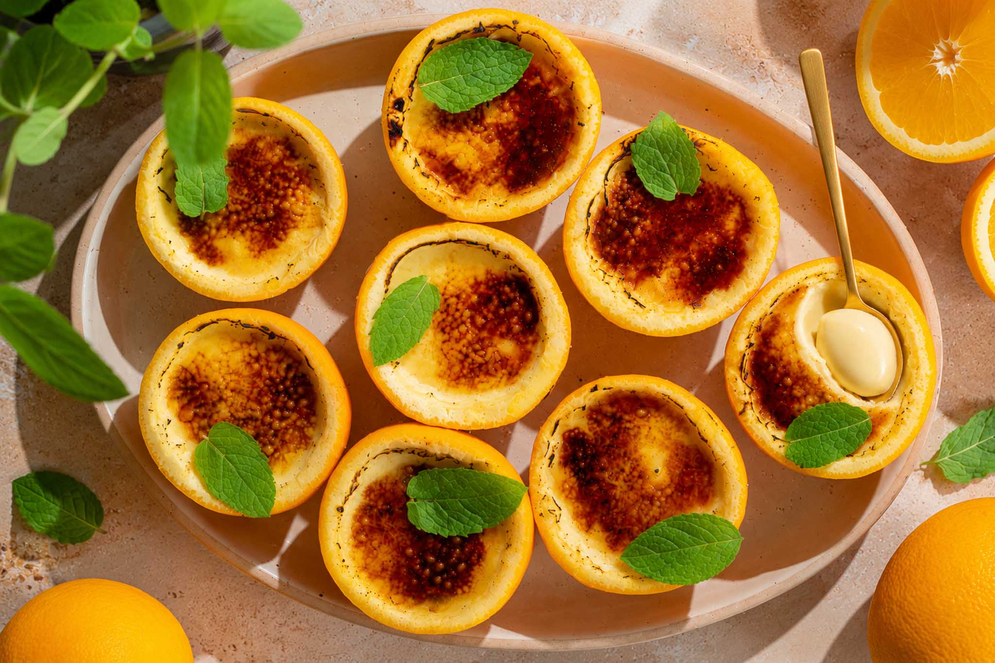 Sinaasappel crème brûlée possets in uitgeholde sinaasappels met een krokante karamellaag en verse munt.