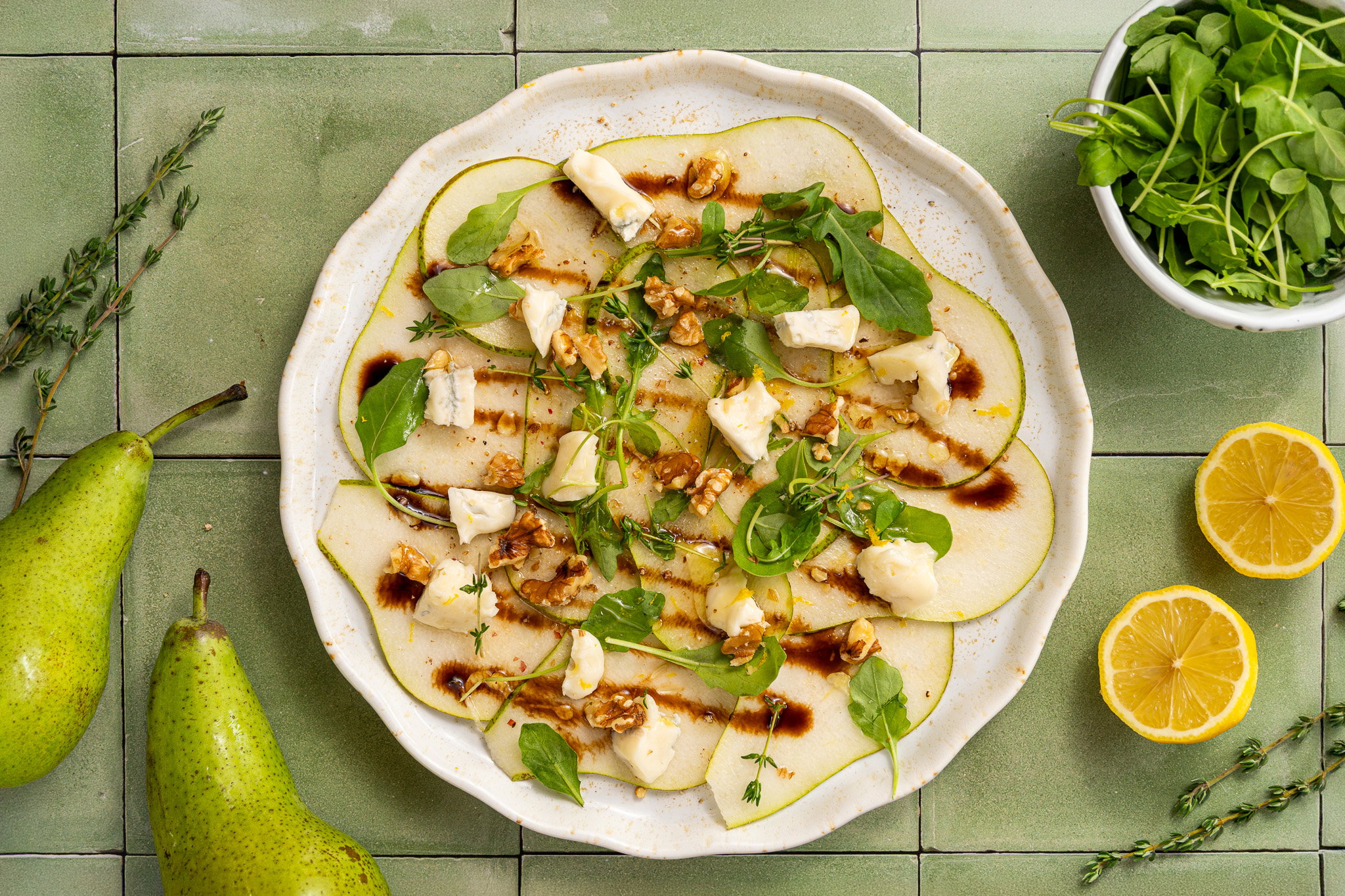 Peer carpaccio met gorgonzola, rucola, geroosterde pecannoten, honing, balsamicocrème en verse tijm.